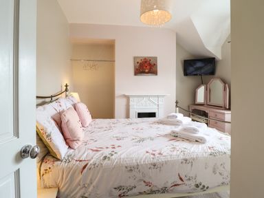 A bedroom with a bed covered in floral bedding and folded towels on top a dressing table with mirrors and a wall-mounted television above at Artro View in Llanbedr