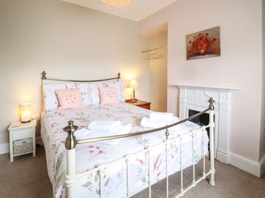 A bedroom with a metal bed frame a bed with floral bedding two bedside tables with lamps a white fireplace and a painting of flowers at Artro View in Llanbedr