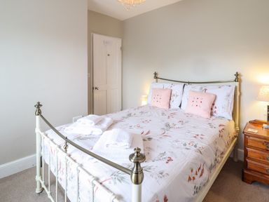 A bedroom with a floral bedspread, two pink pillows, folded towels on the bed, a wooden nightstand with a lamp and books at Artro View in Llanbedr