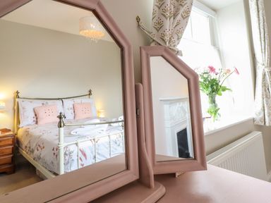 A bedroom with a bed reflected in a pink framed mirror a window with curtains and a flower vase at Artro View in Llanbedr