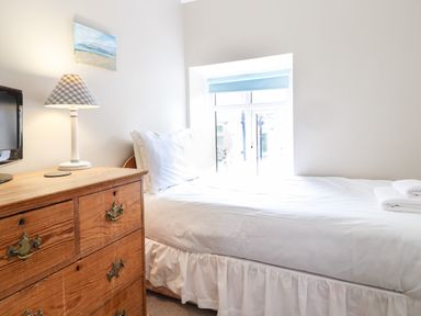 A bedroom with a single bed next to a window and a wooden chest of drawers with a lamp and television at Artro View in Llanbedr