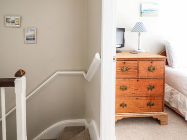 A staircase next to a wooden chest of drawers with a lamp and small television in a bedroom at Artro View in Llanbedr