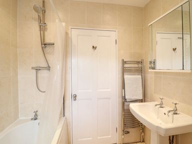 A bathroom with a bathtub shower combination a white door a towel rack with towels a sink and a mirrored cabinet at Artro View in Llanbedr