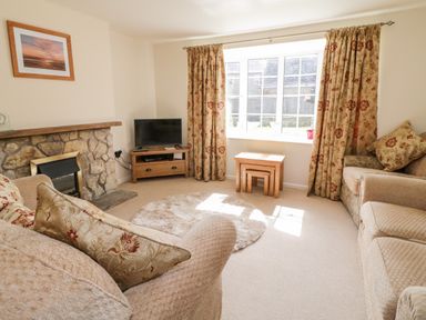 A living room with stone fireplace television wooden tables and patterned curtains at Crooked Well in Timsbury Nr Bath