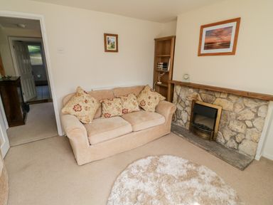 A living room with a beige sofa with floral cushions a stone fireplace a wooden bookshelf and a round shaggy rug at Crooked Well in Timsbury Nr Bath