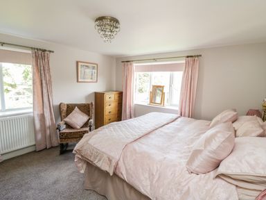 A bedroom with a bed, armchair, dresser, two windows with curtains and a ceiling light at Crooked Well in Timsbury Nr Bath