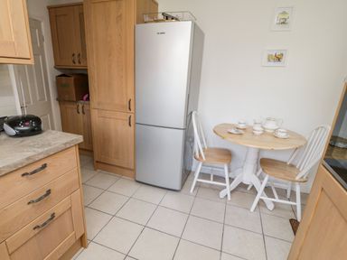 A kitchen with wooden cabinets a silver refrigerator a small round table with two chairs and tea set on the table at Crooked Well Timsbury Nr Bath