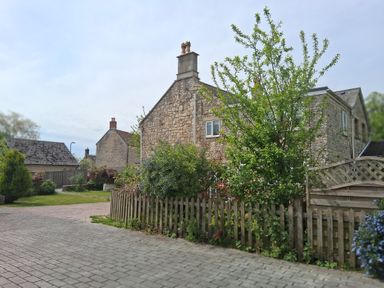 A garden with a stone house and a fence at Crooked Well in Timsbury, Nr Bath