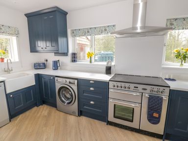 A kitchen with blue cabinets a washing machine a stove and flowers on the windowsill at Orchard House Risbury near Leominster