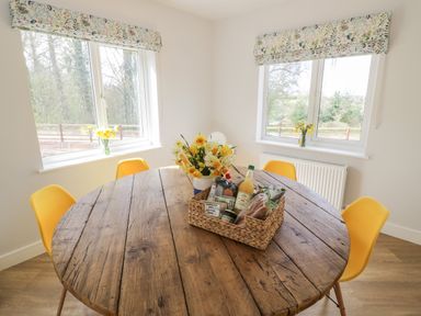 A dining area with a round wooden table yellow chairs and windows with floral blinds at Orchard House Risbury near Leominster