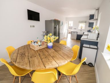A kitchen with a round wooden table surrounded by yellow chairs and a vase of flowers at Orchard House in Risbury near Leominster