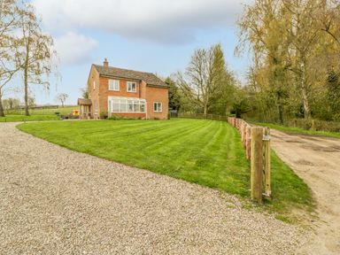 A brick house with a gravel driveway and a green lawn surrounded by trees at Orchard House in Risbury near Leominster
