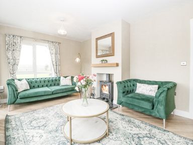 A living room with green sofas a round coffee table with flowers and a fireplace at Orchard House Risbury near Leominster