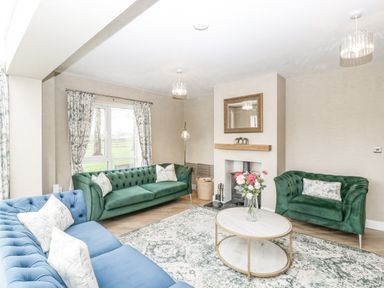 A living room with green and blue sofas a round coffee table and a fireplace at Orchard House in Risbury near Leominster