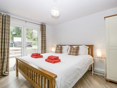 A bedroom with a wooden bed with white bedding and red towels on top two bedside tables with lamps and plaid curtains at Orchard House in Risbury near Leominster