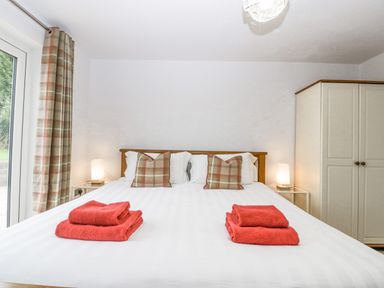 A bedroom with a double bed with red towels on it two plaid pillows two bedside tables with lamps and a wardrobe at Orchard House in Risbury near Leominster