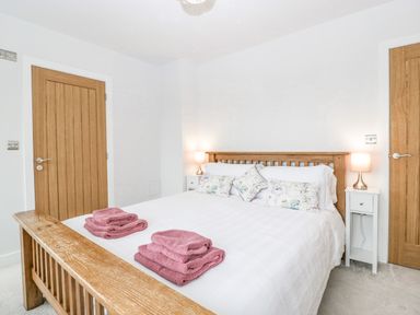 A bedroom with a wooden bed frame white bedding floral pillows two bedside tables with lamps and folded towels on the bed at Orchard House Risbury near Leominster