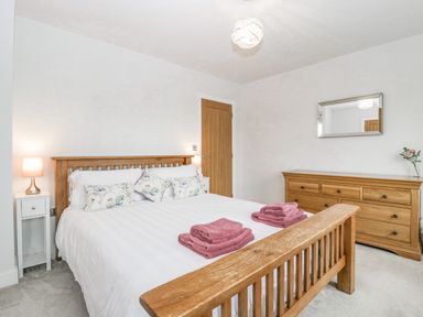 A bedroom with a wooden bed, bedside tables with lamps, a wooden dresser with a mirror, and towels on the bed at Orchard House in Risbury near Leominster