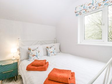 A bedroom with a bed with white linens and floral pillows with orange towels on the bed and a window with floral curtains at Orchard House in Risbury near Leominster
