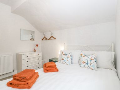 A bedroom with a bed with orange towels and patterned cushions a white dresser with a flower a wall mirror and wooden hangers on hooks at Orchard House Risbury near Leominster