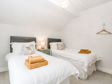 A bedroom with two single beds side by side with white bedding an ornate pillow and folded towels at Orchard House in Risbury near Leominster
