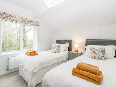 A bedroom with two single beds white bedding floral cushions and folded orange towels at Orchard House in Risbury near Leominster