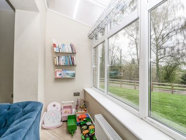 A corner with children's toys and books next to large windows overlooking grass at Orchard House in Risbury near Leominster