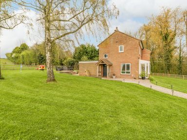 A brick house with a path and green lawn surrounded by trees at Orchard House in Risbury near Leominster
