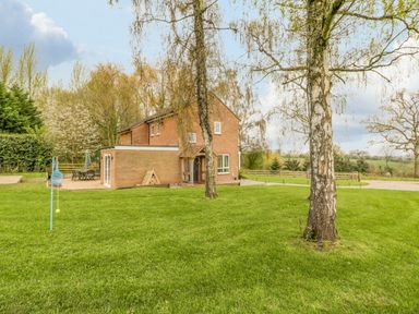 A brick house with a patio and outdoor furniture in a grassy garden with trees at Orchard House in Risbury near Leominster