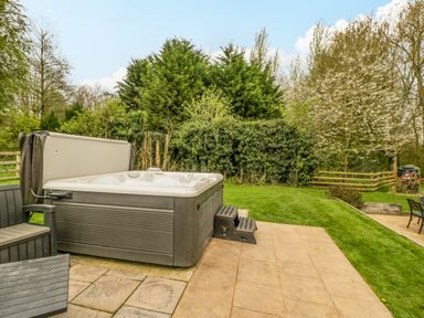 An outdoor hot tub on a paved patio next to a lawn with trees and a wooden fence at Orchard House in Risbury near Leominster
