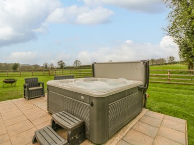 An outdoor patio with a hot tub small steps two plastic chairs a fire pit and a fenced grassy area at Orchard House in Risbury near Leominster