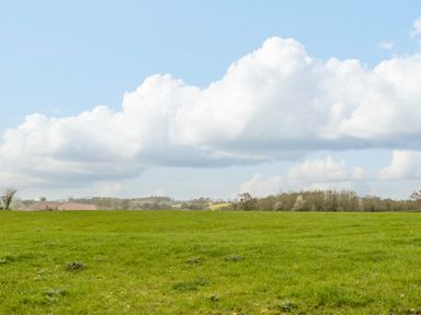 A green grassy field with trees and a cloudy blue sky at Orchard House in Risbury near Leominster