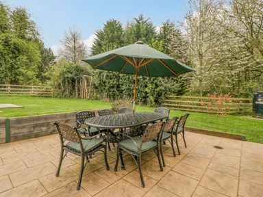An outdoor patio with a table, eight chairs, and a large umbrella surrounded by grass and trees at Orchard House in Risbury near Leominster
