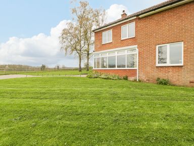 A brick house with multiple windows and a large grassy lawn with trees and a fence at Orchard House in Risbury near Leominster
