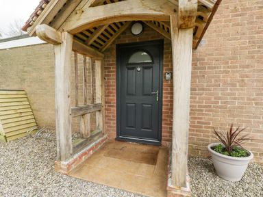 A front porch with wooden beams a black door a doormat and a potted plant at Orchard House in Risbury near Leominster