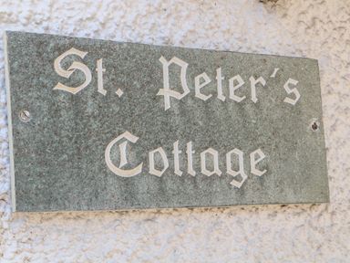 A stone plaque with the text St Peters Cottage mounted on a textured wall at St Peters Cottage in Milnthorpe