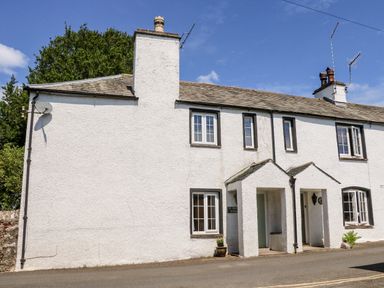 A white two story cottage with multiple windows and two porch entrances at St Peters Cottage in Milnthorpe