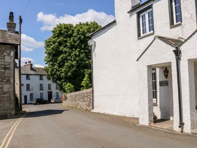 A street view with white buildings trees and parked cars at St Peters Cottage in Milnthorpe