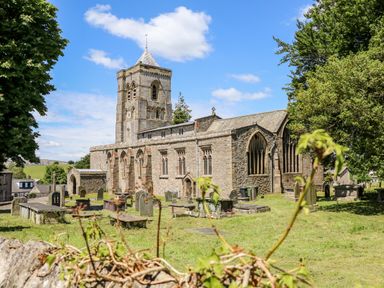 A stone church with a tower and arched windows surrounded by gravestones and trees at St Peters Cottage in Milnthorpe