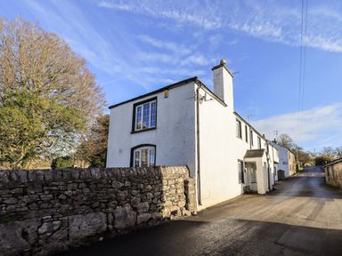 A white house with a stone wall in front and a road beside it at St Peters Cottage in Milnthorpe