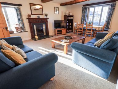 A living room with blue sofas a wooden coffee table fireplace television dining table and chairs at St Peters Cottage in Milnthorpe