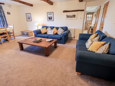 A living room with two blue sofas with cushions a wooden coffee table and dining table with chairs at St Peters Cottage in Milnthorpe