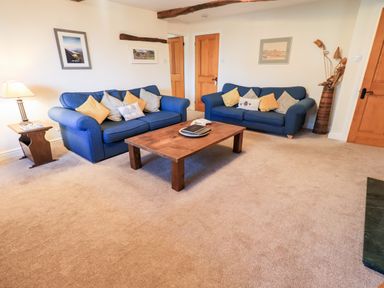 A living room with two blue sofas a wooden coffee table and framed pictures on the wall at St Peters Cottage in Milnthorpe