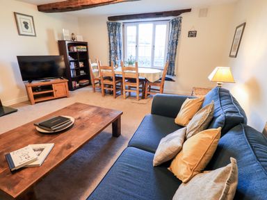 A living room with a blue sofa pillows wooden coffee table dining table chairs television and bookshelf at St Peters Cottage Milnthorpe