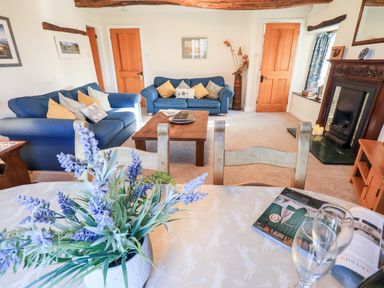 A living room with blue sofas, wooden coffee table, fireplace, dining table with flowers and chairs at St Peters Cottage in Milnthorpe