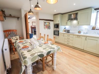 A kitchen with a dining table set for breakfast and wooden chairs at St Peters Cottage in Milnthorpe
