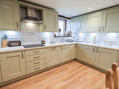 A kitchen with light green cabinets white countertops a stainless steel hood and wooden floor at St Peters Cottage in Milnthorpe