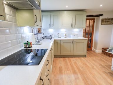 A kitchen with light green cabinets white countertops a stove and a door leading to another room at St Peters Cottage in Milnthorpe