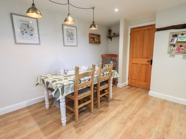 A dining room with a table covered by a patterned tablecloth and three wooden chairs at St Peters Cottage in Milnthorpe