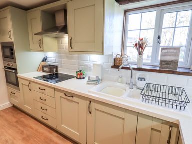 A kitchen with cabinets a sink a window and an induction cooktop at St Peters Cottage in Milnthorpe